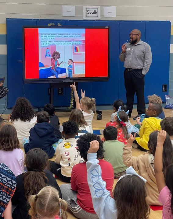 An author reading a picture book aloud to a circle of schoolchildren